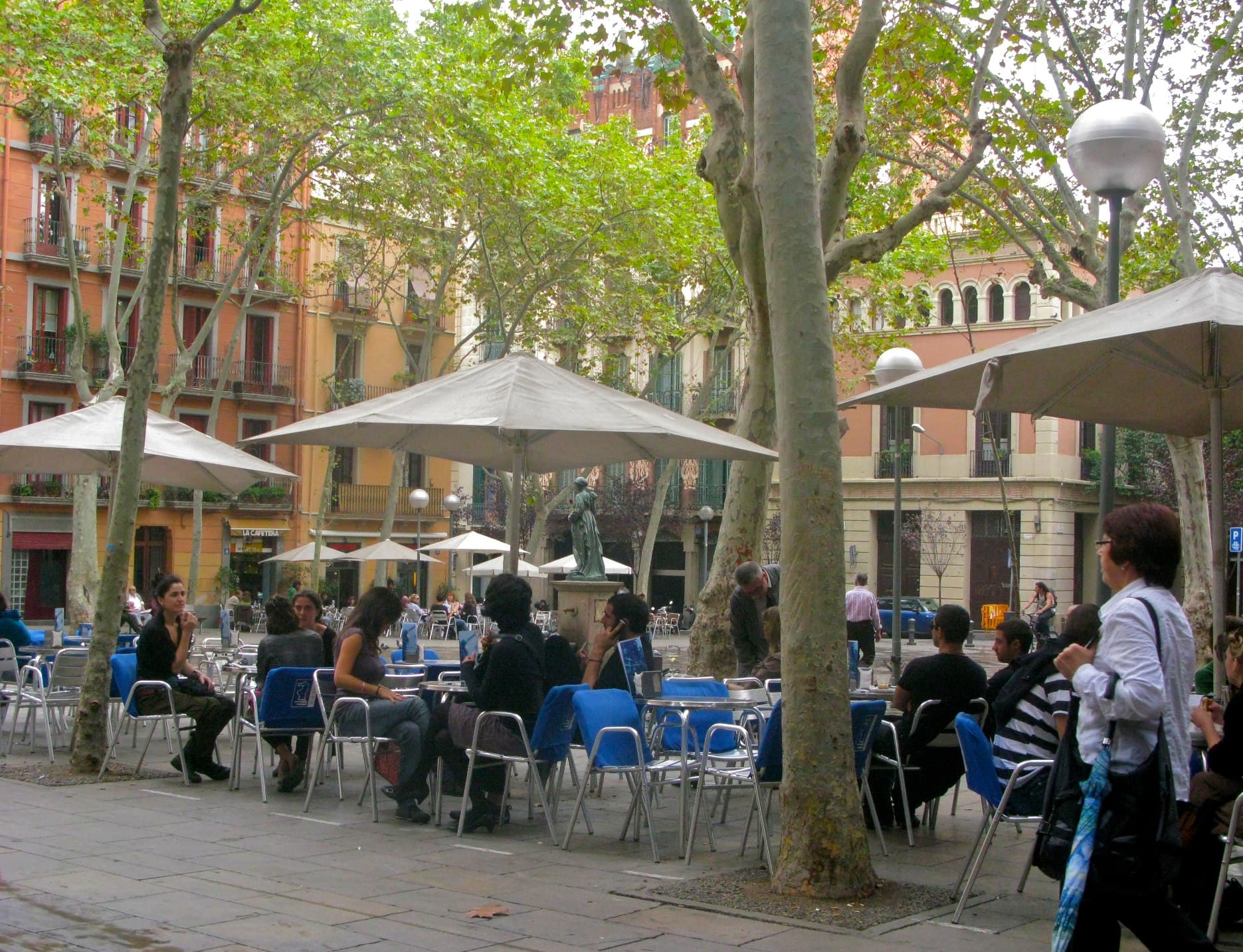 Terrassa a la plaça de la Virreina, Gràcia, Barcelona; persones assegudes al voltant de taules sota els arbres.